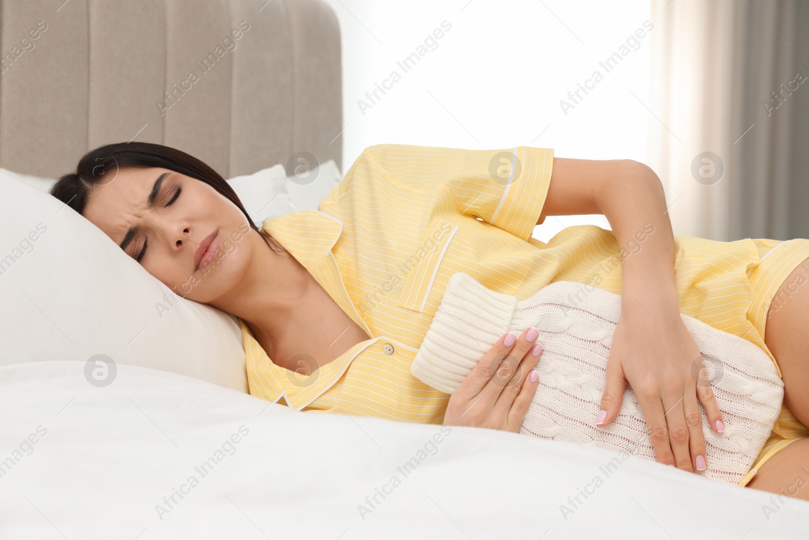 Photo of Woman using hot water bottle to relieve menstrual pain on bed at home