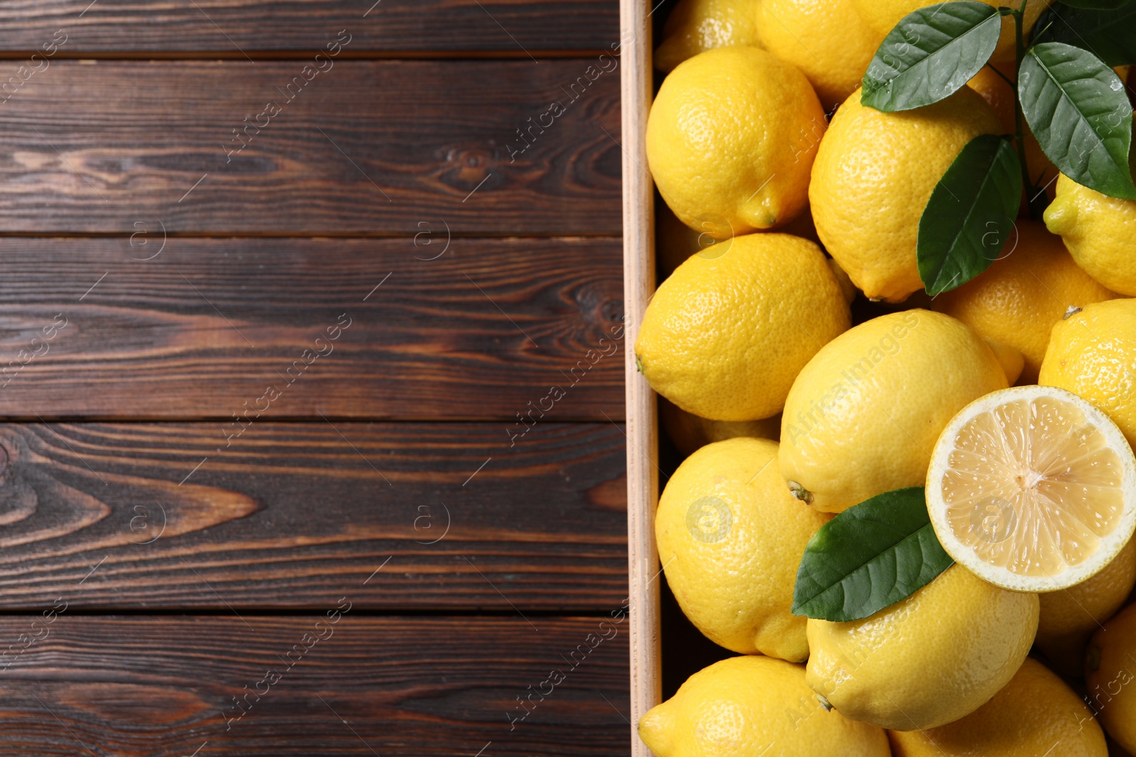 Photo of Fresh lemons in crate on wooden table, top view. Space for text