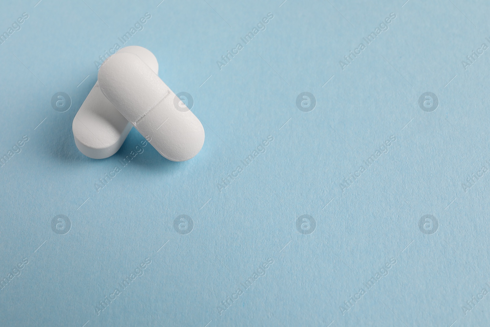 Photo of Two white pills on light blue background, closeup. Space for text