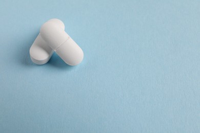 Two white pills on light blue background, closeup. Space for text