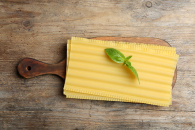 Photo of Uncooked lasagna sheets with basil on wooden table, top view