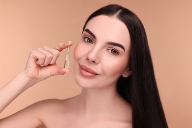 Photo of Beautiful young woman holding skincare ampoule on beige background