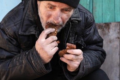 Poor homeless man holding piece of bread outdoors