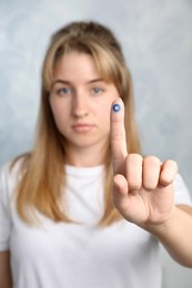Photo of Woman showing finger with drawn blue circle against color background, focus on hand. World Diabetes Day
