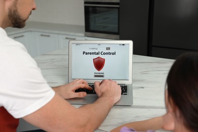 Dad installing parental control on laptop at table in kitchen, closeup. Child safety