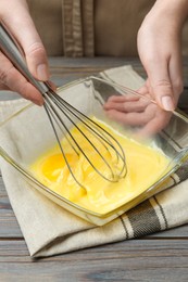 Photo of Woman whisking eggs in glass bowl at wooden table, closeup