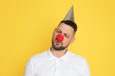 Funny man with clown nose and party hat on yellow background. April fool's day