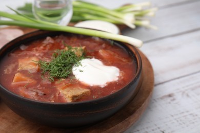 Tasty borscht with sour cream in bowl served with green onion on white wooden table, closeup. Space for text