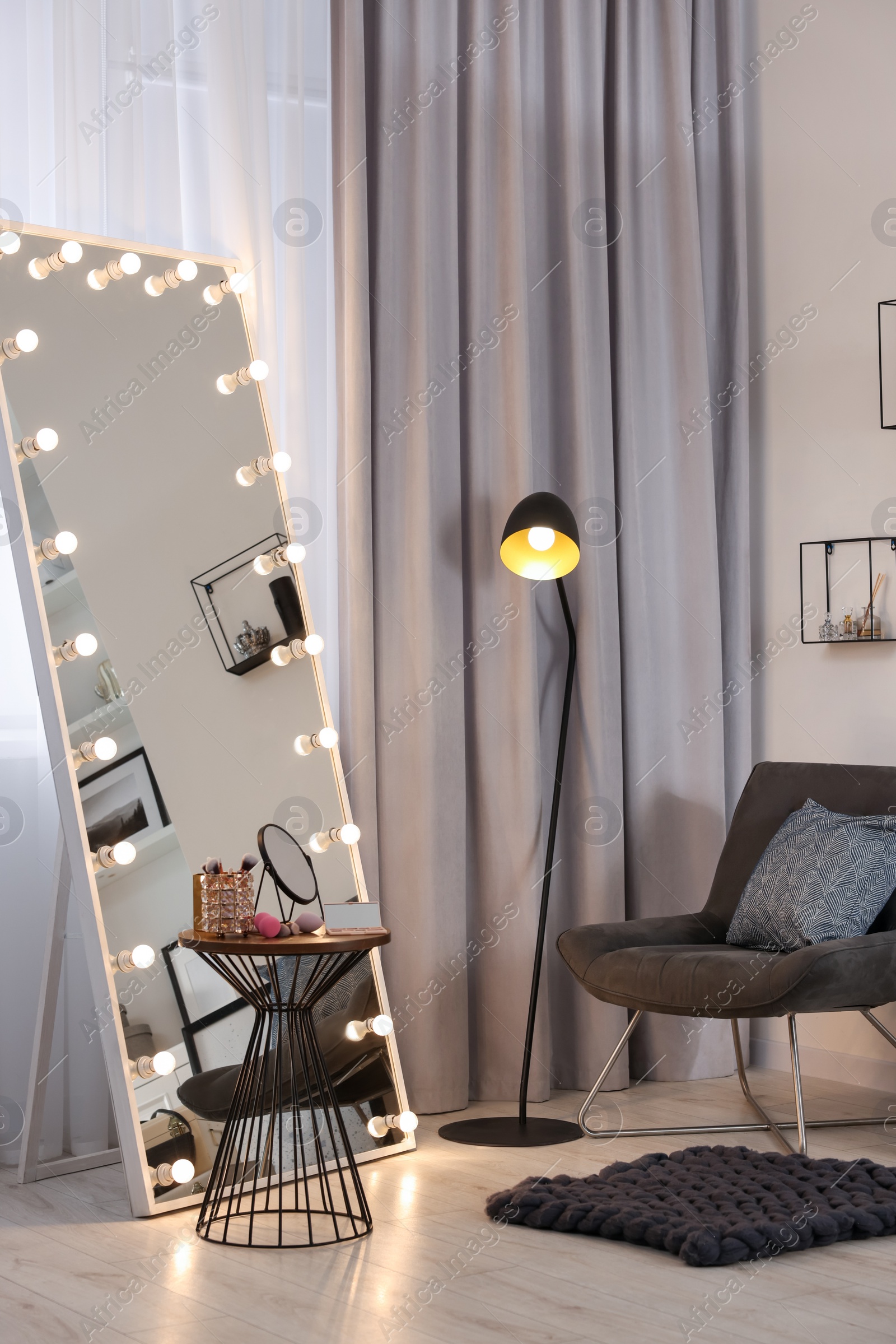 Photo of Makeup room. Stylish mirror with light bulbs, beauty products on table and armchair indoors