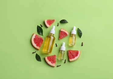 Photo of Flat lay composition with bottles of grapefruit essential oil on green background
