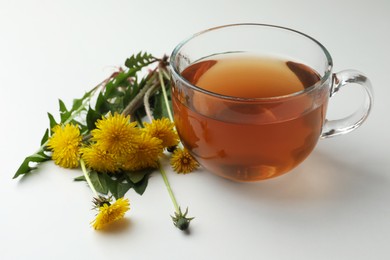 Photo of Delicious fresh tea and beautiful dandelion flowers on white background