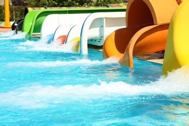 Different colorful slides and swimming pool in water park on sunny day