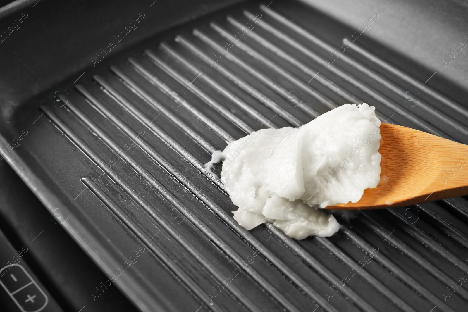 Photo of Wooden spoon with coconut oil in frying pan, closeup. Healthy cooking