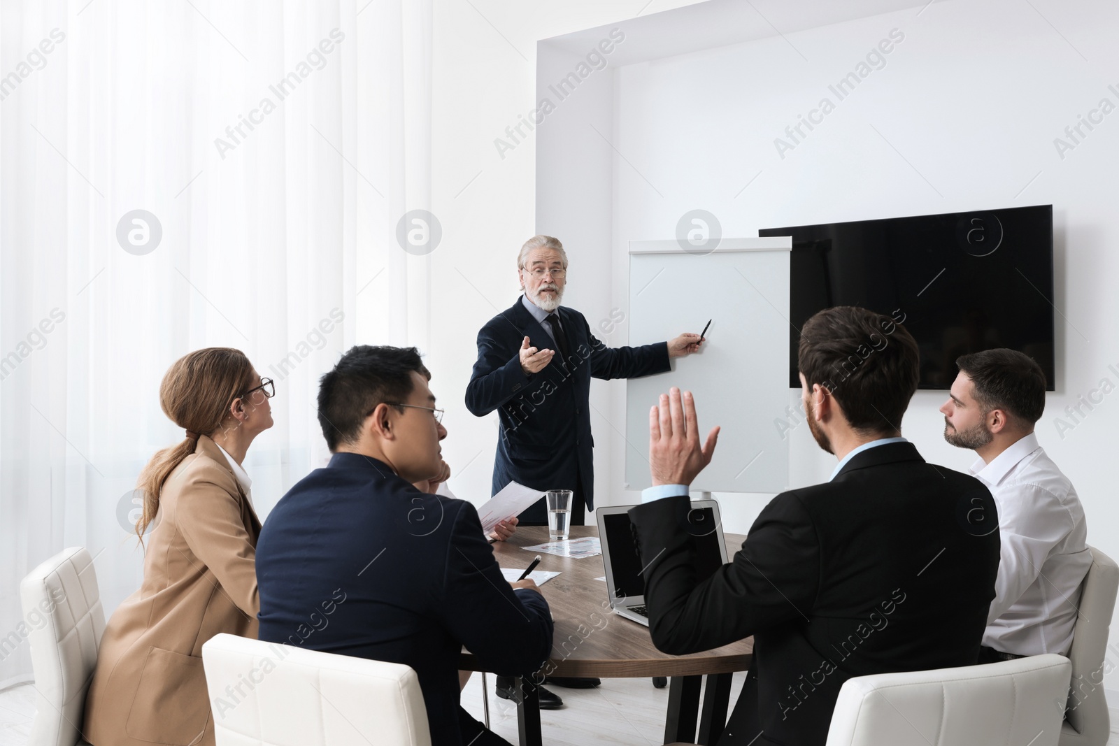 Photo of Business conference. Group of people listening to senior speaker report near tv screen in meeting room