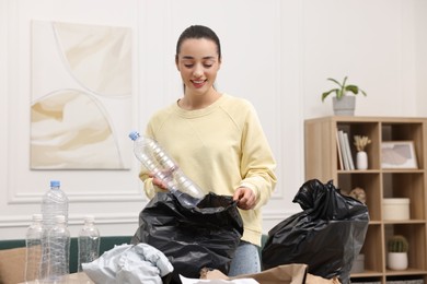 Photo of Smiling woman with plastic bag separating garbage in room