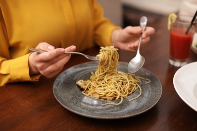 Young woman eating tasty pasta carbonara at restaurant, closeup view