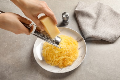Photo of Woman grating cheese onto cooked spaghetti squash on table, closeup
