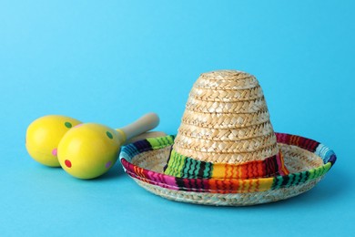 Photo of Mexican sombrero hat and maracas on light blue background