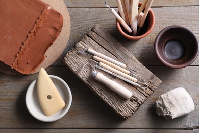 Clay and set of modeling tools on wooden table, flat lay