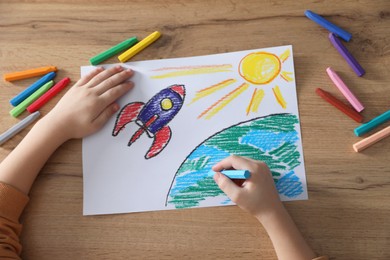 Photo of Little girl drawing picture with soft pastel at wooden table, top view. Child`s art