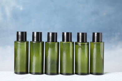 Mini bottles with cosmetic products on white table against blue background