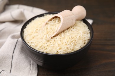 Photo of Bowl and scoop with raw rice on wooden table, closeup