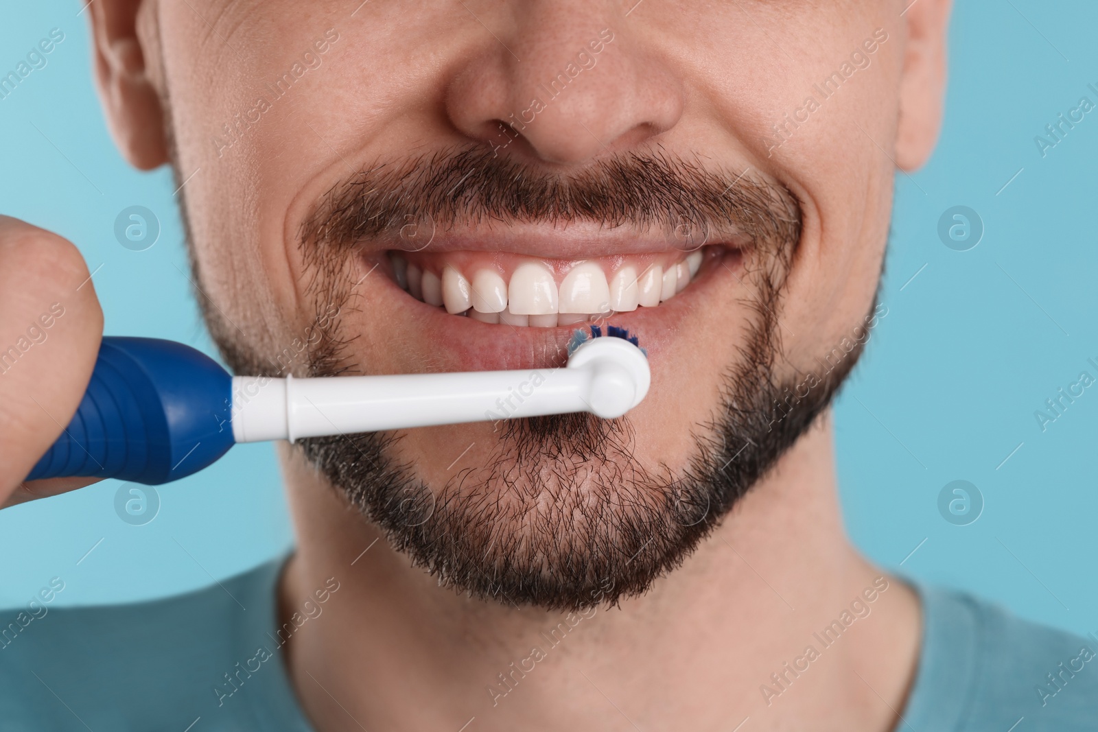 Photo of Man brushing his teeth with electric toothbrush on light blue background, closeup