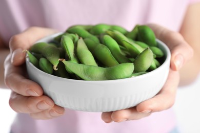 Photo of Woman holding bowl with green edamame beans in pods on white background, closeup