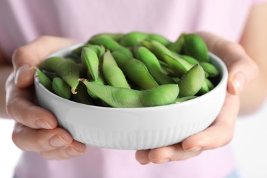 Woman holding bowl with green edamame beans in pods on white background, closeup