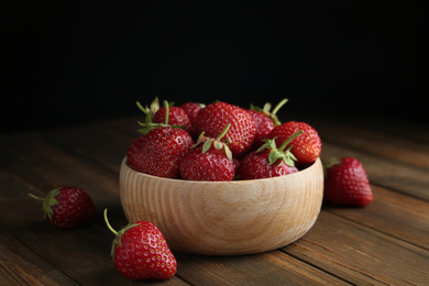 Photo of Delicious ripe strawberries in bowl on wooden table