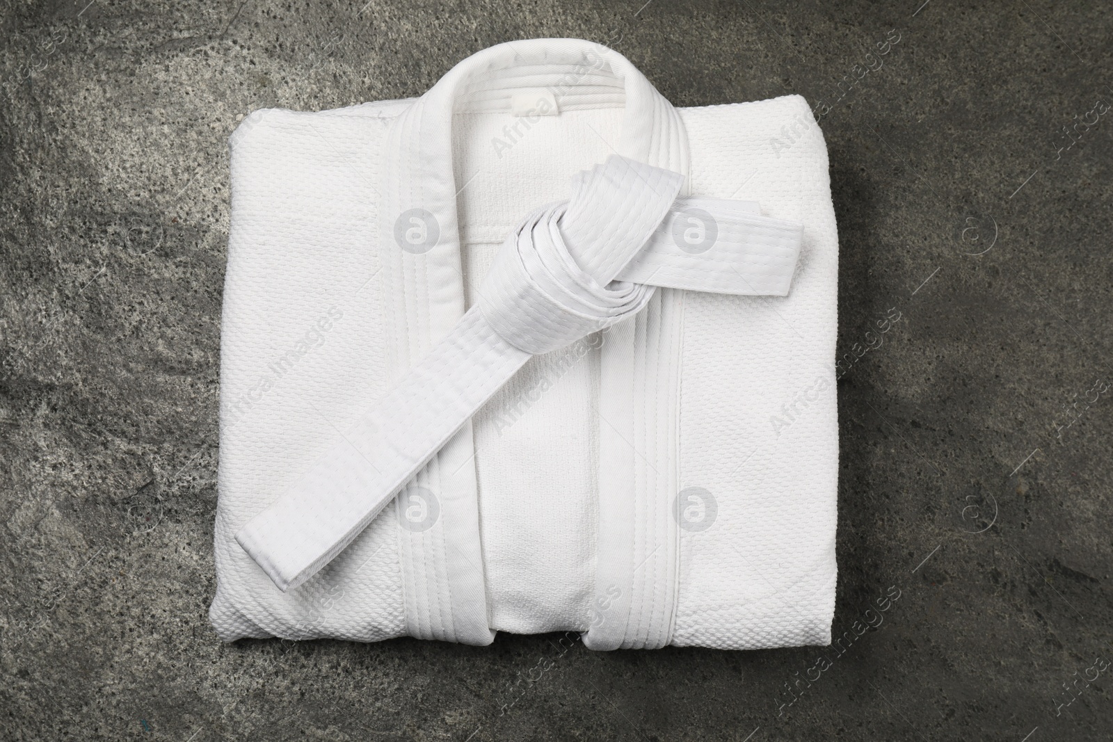 Photo of White karate belt and kimono on gray textured background, top view