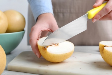 Photo of Woman cutting ripe apple pear at table, closeup