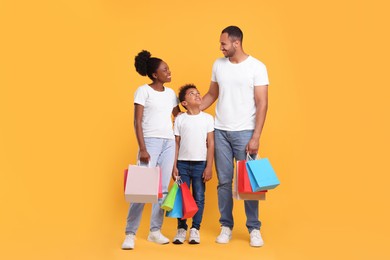 Photo of Family shopping. Happy parents and son with colorful bags on orange background