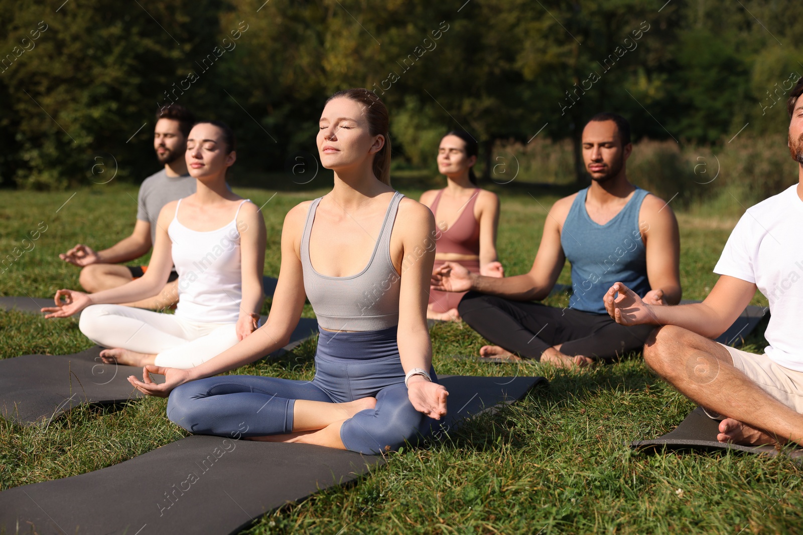 Photo of Group of people practicing yoga on mats outdoors. Lotus pose