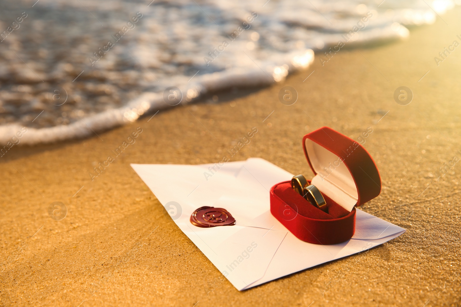 Photo of Red box with gold wedding rings and envelope on sandy beach