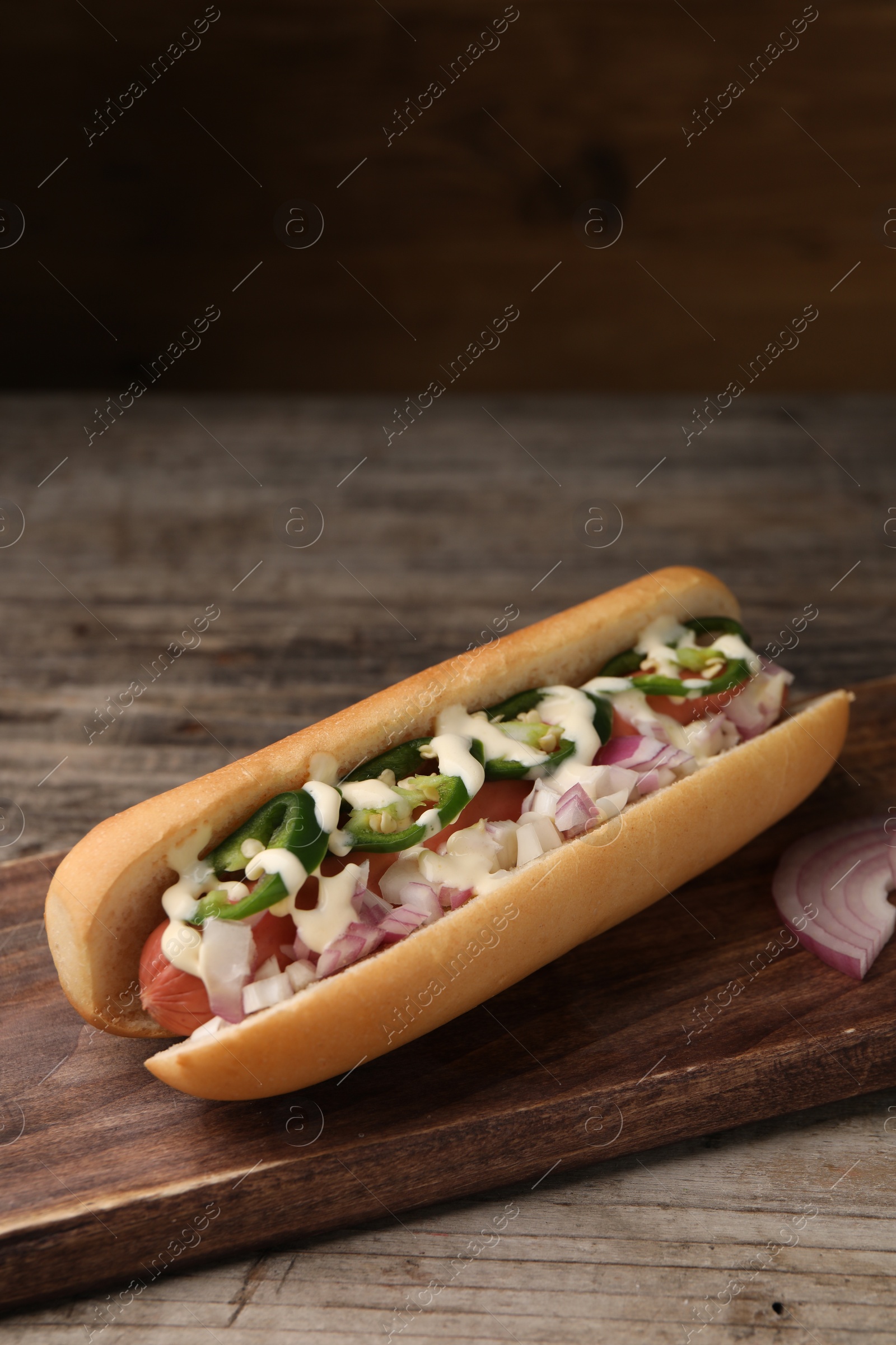 Photo of Delicious hot dog with onion, chili pepper and sauce on wooden table, space for text