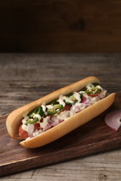 Delicious hot dog with onion, chili pepper and sauce on wooden table, space for text