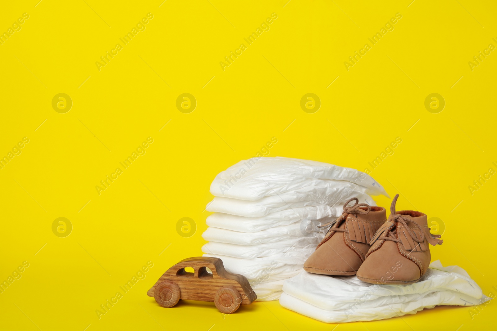 Photo of Diapers, toy car and baby shoes on yellow background. Space for text
