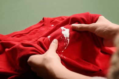 Photo of Woman holding red shirt with white paint stain on green background, closeup