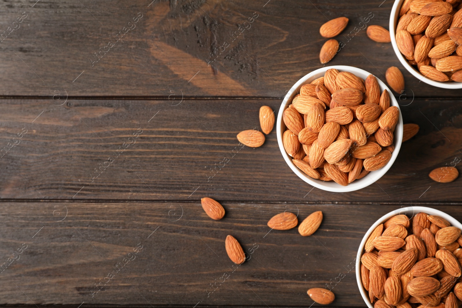 Photo of Tasty organic almond nuts in bowls and space for text on table, top view