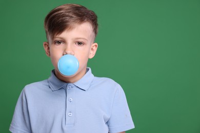 Boy blowing bubble gum on green background, space for text