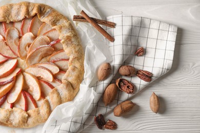 Photo of Delicious apple galette, cinnamon and pecans on white wooden table, flat lay