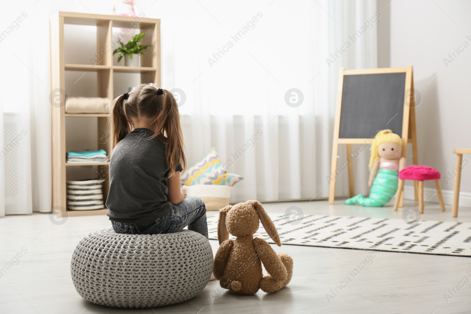 Photo of Lonely little girl with toy bunny at home, back view. Autism concept