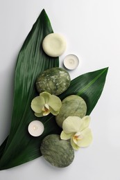 Flat lay composition with spa stones, green leaves and beautiful flowers on white table