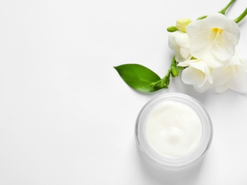 Photo of Jar of cream and flowers on white background, top view. Professional cosmetic products