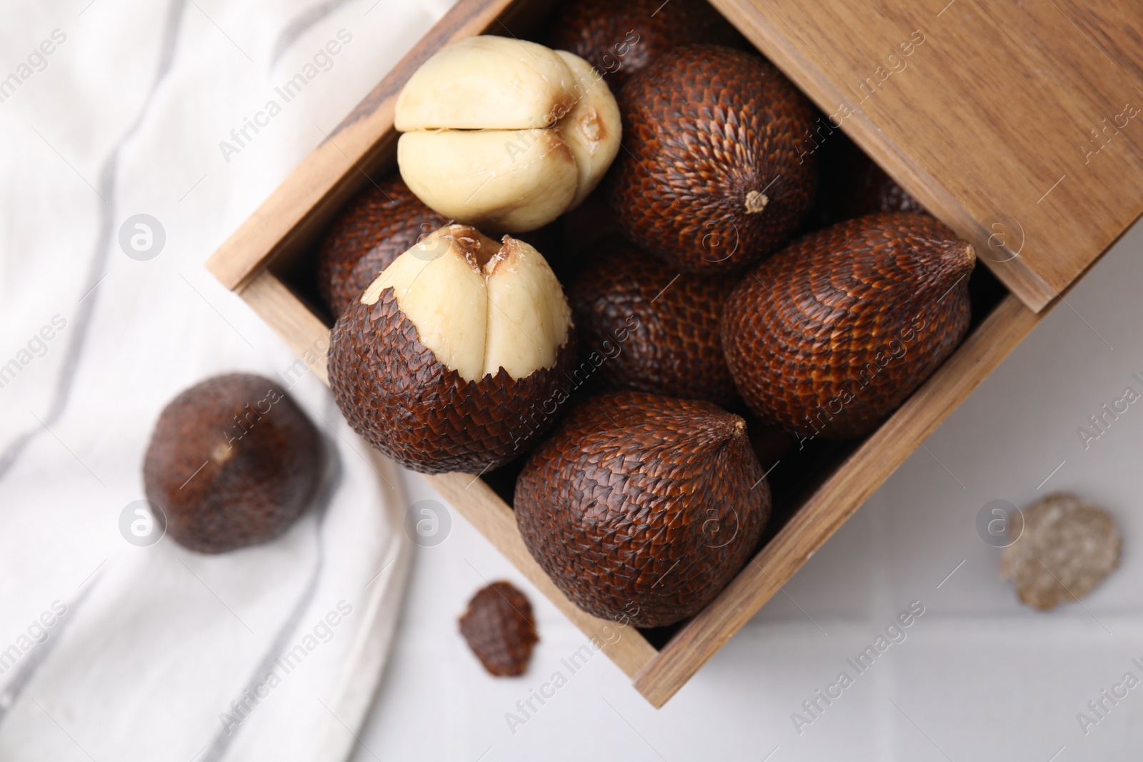 Photo of Wooden crate with fresh salak fruits on white tiled table, top view
