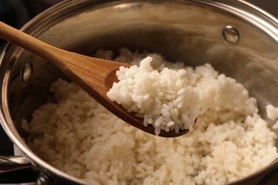 Wooden spoon with delicious rice over pot, closeup