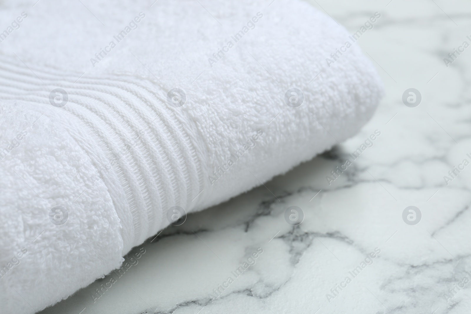 Photo of Folded terry towel on white marble table, closeup. Space for text