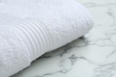 Folded terry towel on white marble table, closeup. Space for text