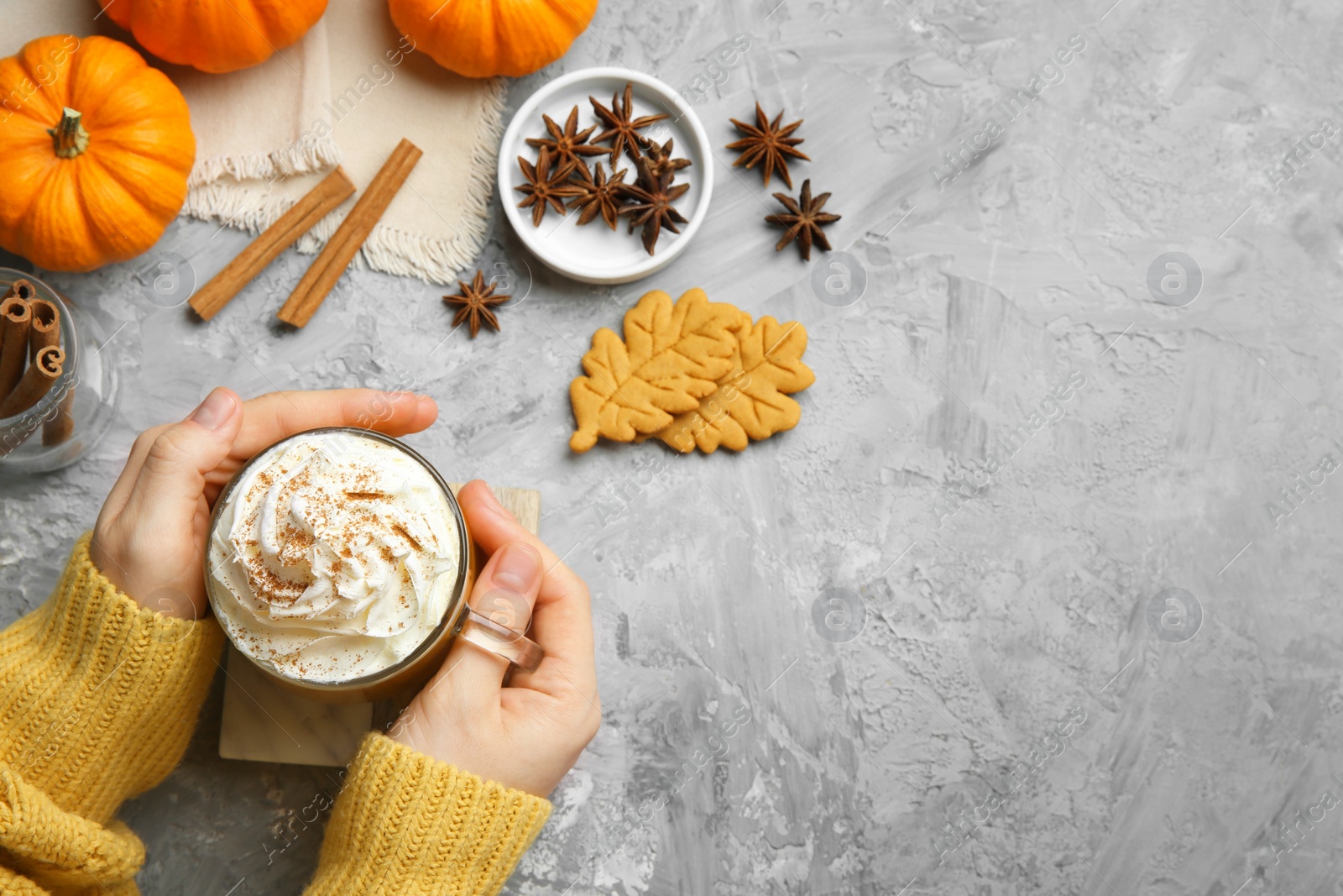 Photo of Woman holding cup of pumpkin spice latte with whipped cream at light grey table, top view. Space for text